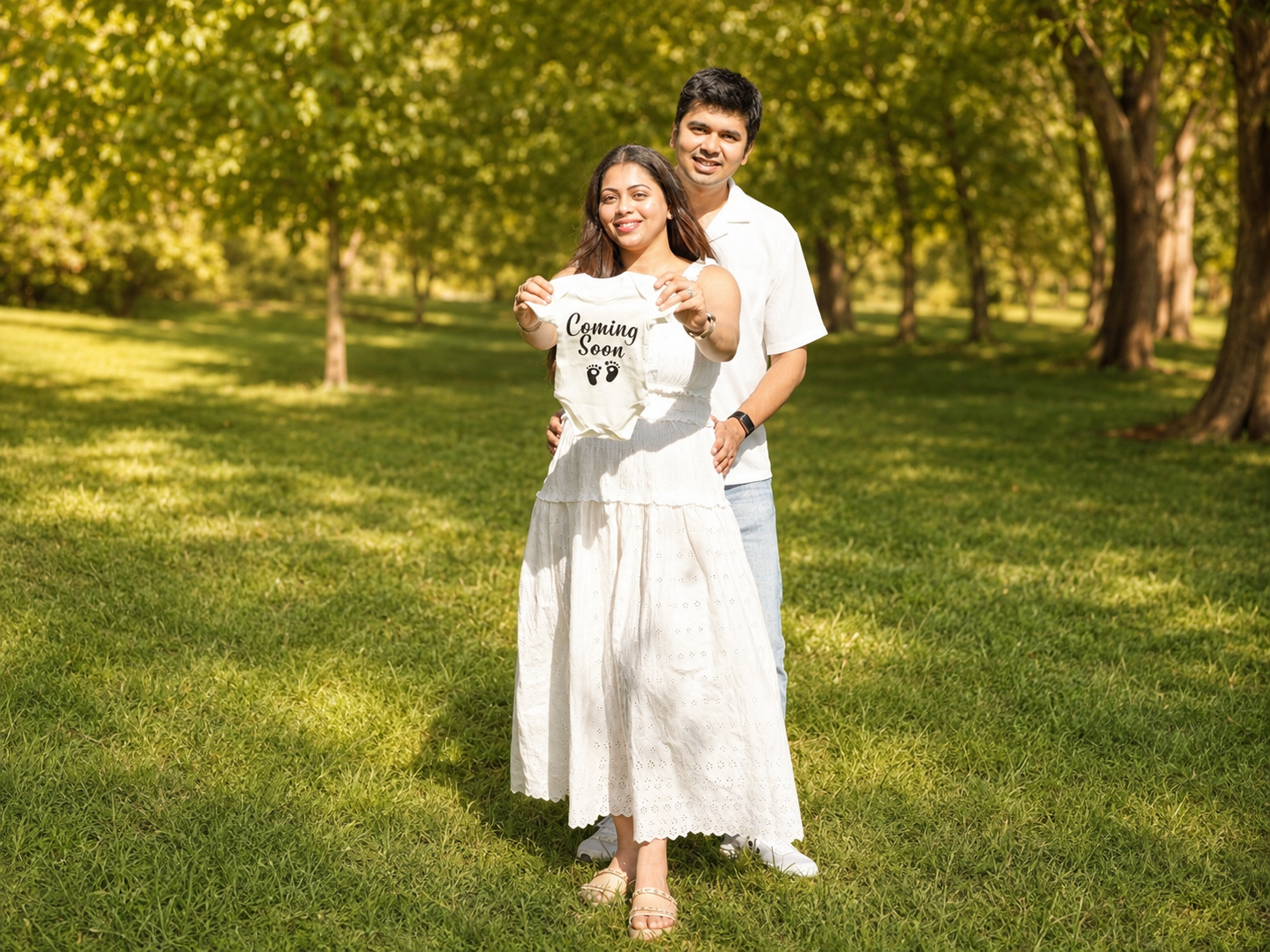Dhwani and Dharam holding a 'Coming soon' onesie in a sunlit park