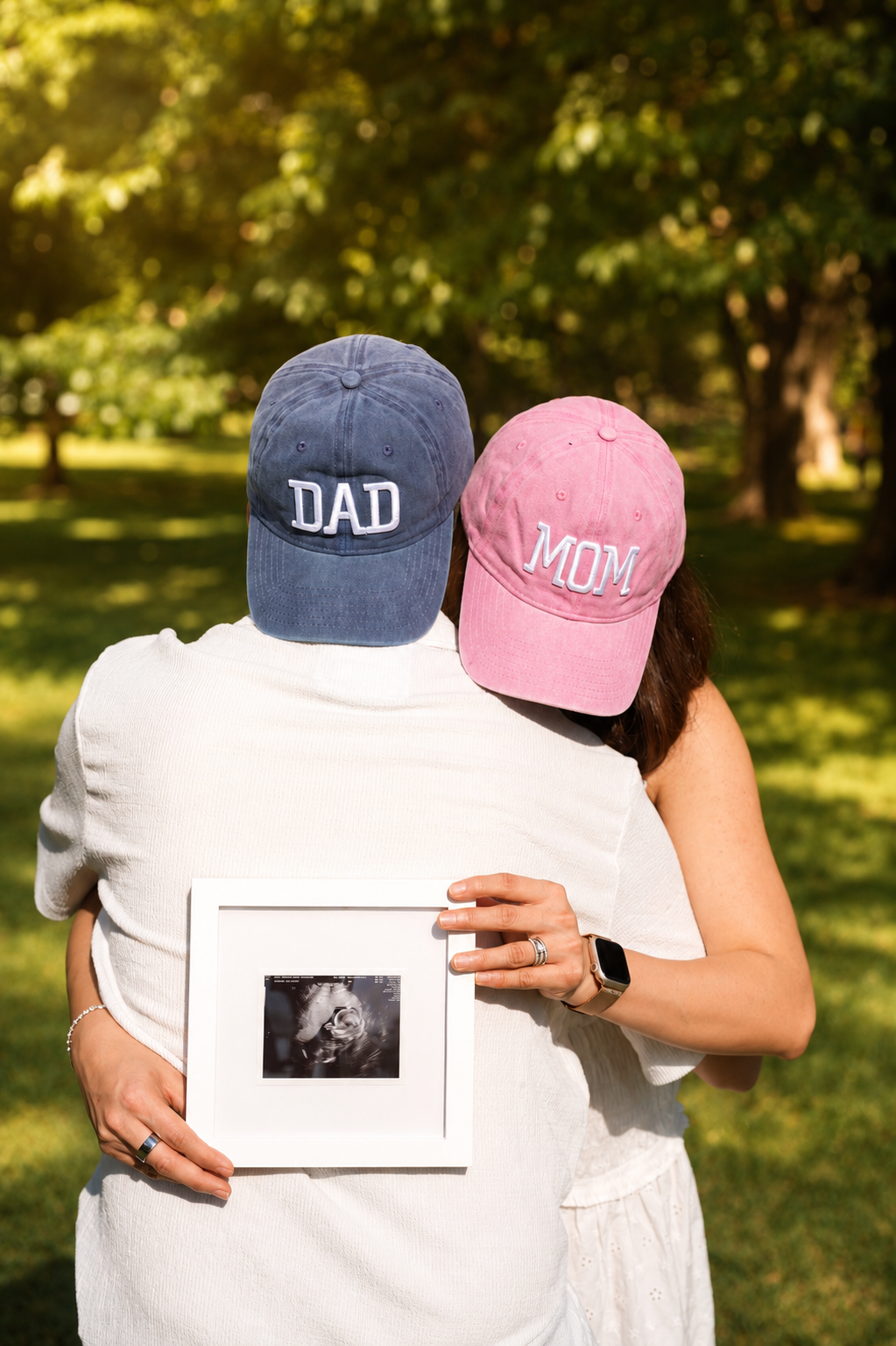 Couple from behind wearing 'Mom' and 'Dad' caps, holding the first ultrasound