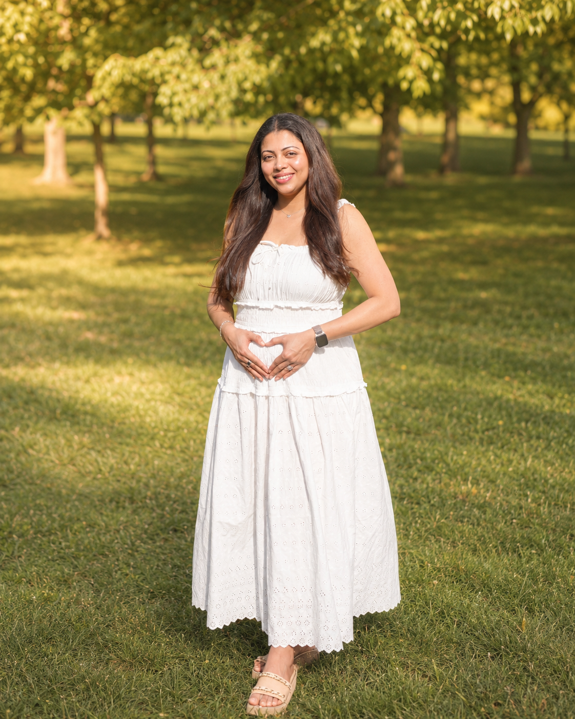 Dhwani in a white dress, hands forming a heart on her bump